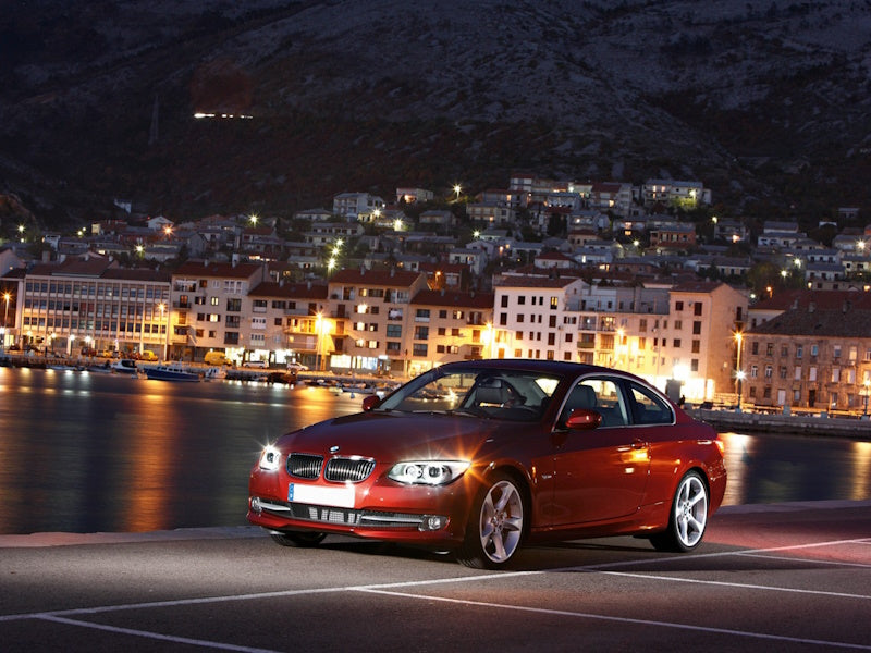 Red car parked by waterfront at night.
