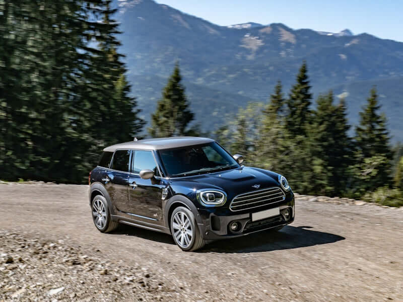 Black Mini Cooper on a dirt road with mountain backdrop.